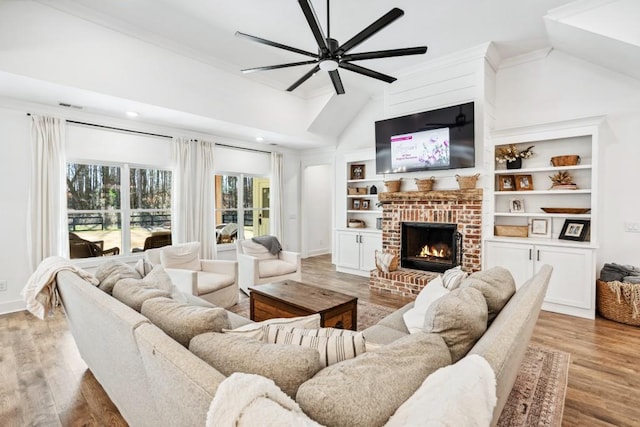 living room featuring ceiling fan, high vaulted ceiling, light hardwood / wood-style floors, a brick fireplace, and built in shelves