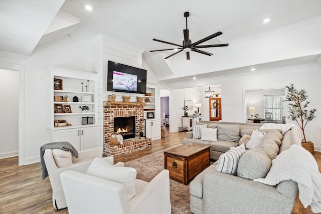 living room featuring high vaulted ceiling, a fireplace, ceiling fan, light hardwood / wood-style floors, and crown molding