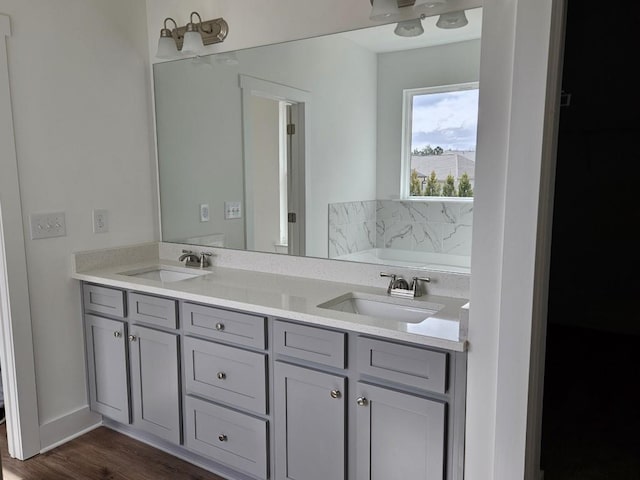 bathroom with wood finished floors, a garden tub, a sink, and double vanity