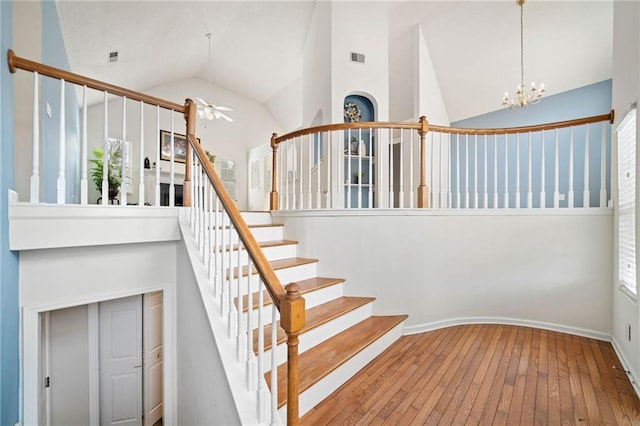 stairway with hardwood / wood-style flooring, high vaulted ceiling, and ceiling fan with notable chandelier