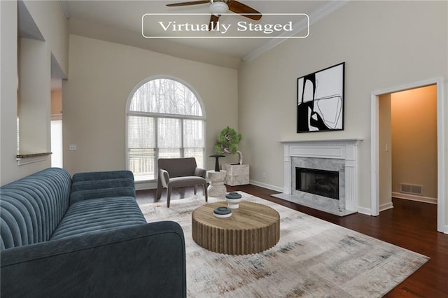 living room with a fireplace, ceiling fan, ornamental molding, and dark wood-type flooring