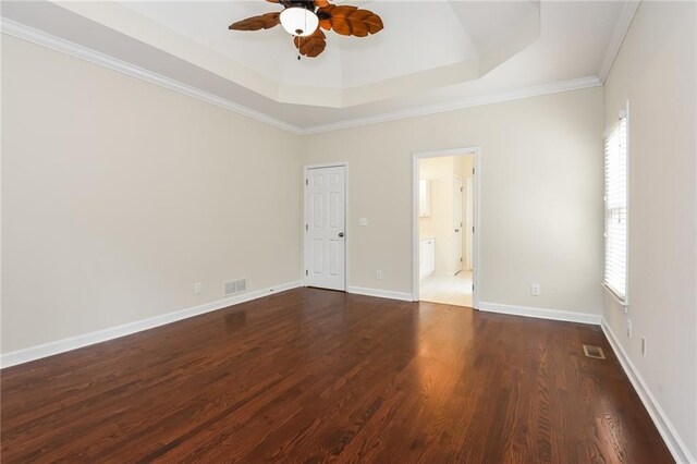 empty room with a raised ceiling, ornamental molding, plenty of natural light, and dark wood-type flooring