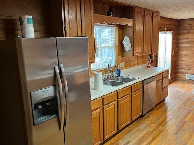 kitchen featuring a sink, a textured ceiling, stainless steel appliances, wood walls, and light countertops