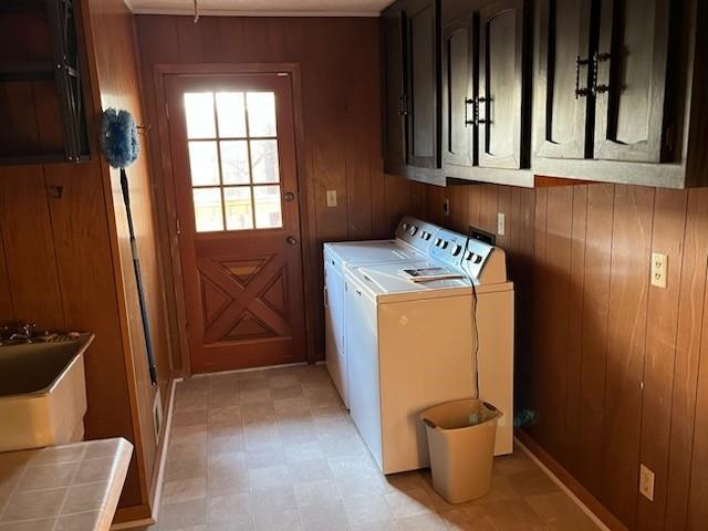 washroom featuring washing machine and dryer, cabinet space, and wood walls
