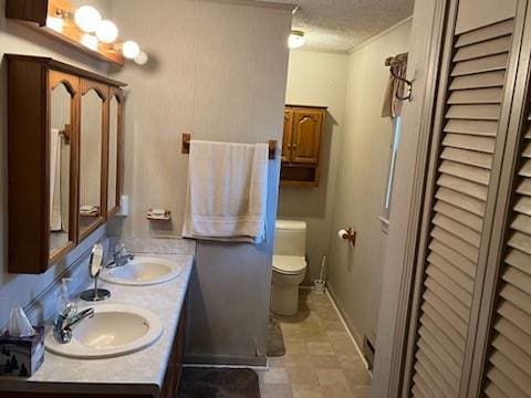 bathroom with a textured ceiling, double vanity, toilet, and a sink