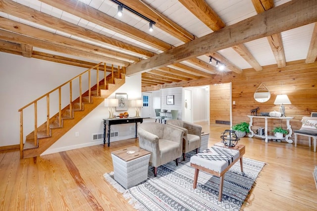 living room featuring rail lighting, wooden walls, beamed ceiling, light hardwood / wood-style floors, and wood ceiling