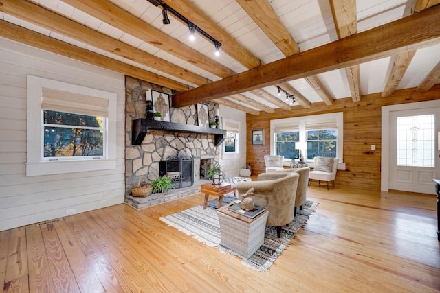 living room with beam ceiling, wood walls, light hardwood / wood-style floors, track lighting, and a fireplace