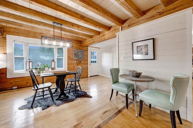 dining area featuring wood ceiling, beam ceiling, light wood-type flooring, and wooden walls