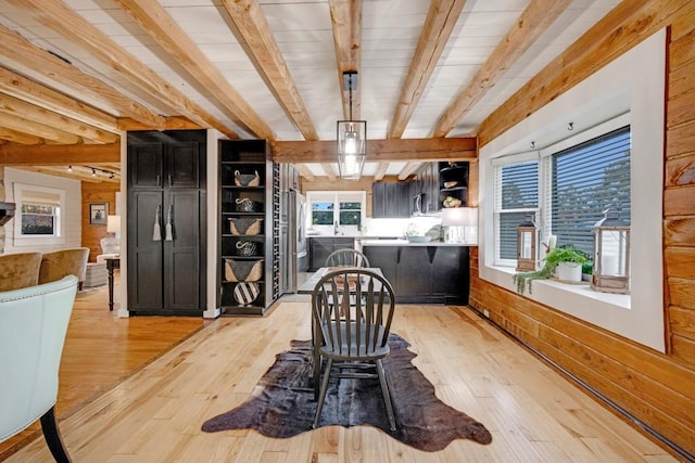 dining space with beamed ceiling, light hardwood / wood-style floors, and wooden walls