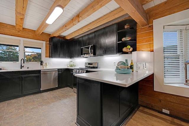 kitchen featuring sink, wooden walls, beamed ceiling, kitchen peninsula, and stainless steel appliances