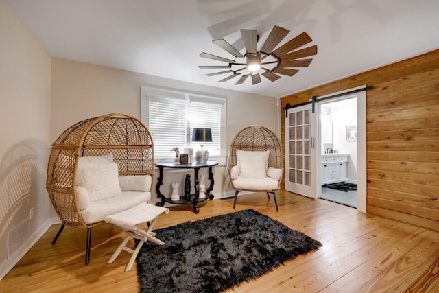 living area featuring a barn door, hardwood / wood-style flooring, ceiling fan, and wood walls