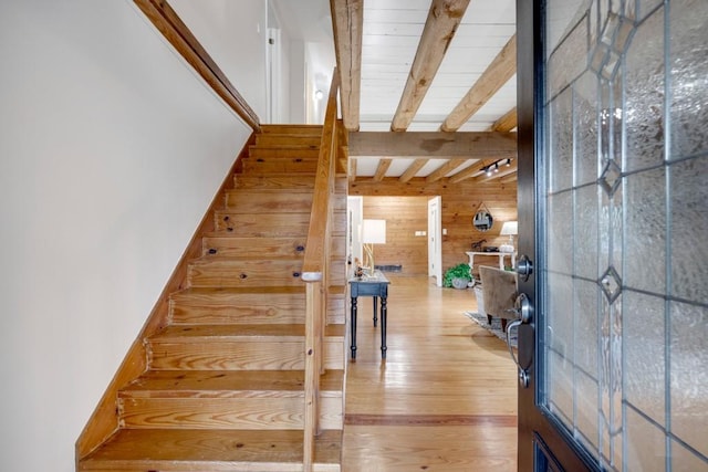 stairway with wood walls, hardwood / wood-style floors, and beamed ceiling