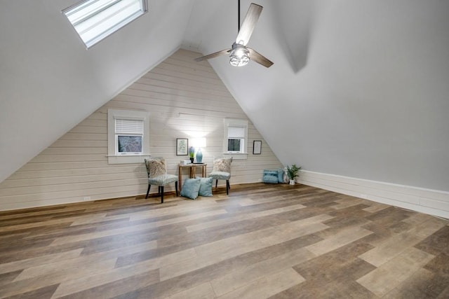 unfurnished room featuring hardwood / wood-style floors, ceiling fan, wood walls, and lofted ceiling with skylight