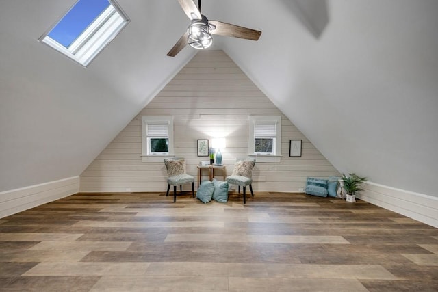 sitting room with vaulted ceiling with skylight, ceiling fan, hardwood / wood-style floors, and wooden walls