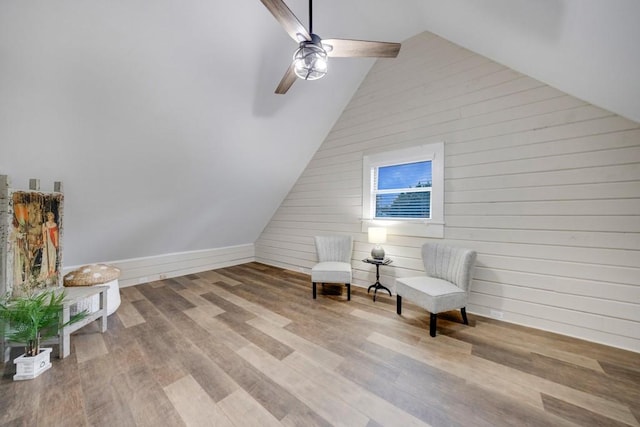 sitting room with wood walls, light hardwood / wood-style flooring, ceiling fan, and lofted ceiling