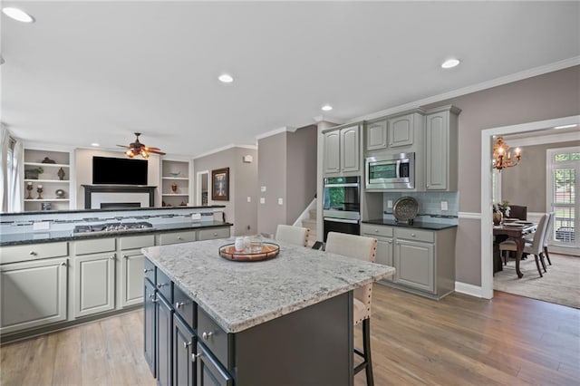 kitchen with gray cabinetry, appliances with stainless steel finishes, ornamental molding, and a kitchen breakfast bar