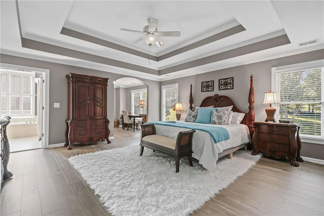 bedroom featuring light wood-style floors, arched walkways, a tray ceiling, visible vents, and ornamental molding