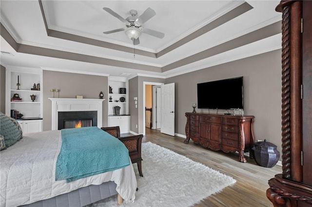 bedroom featuring ornamental molding, a lit fireplace, a tray ceiling, and wood finished floors