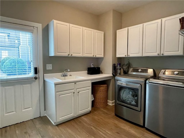 laundry room with washing machine and clothes dryer, cabinet space, a sink, light wood-style floors, and baseboards