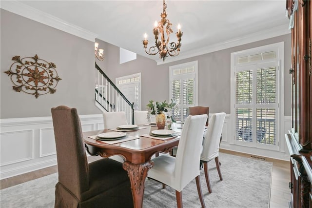 dining space with crown molding, a decorative wall, a chandelier, light wood-type flooring, and stairway