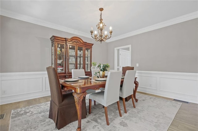 dining area featuring an inviting chandelier, crown molding, wood finished floors, and visible vents