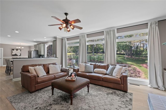 living area featuring recessed lighting, a wealth of natural light, ceiling fan with notable chandelier, and light wood-type flooring