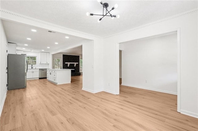unfurnished living room with an inviting chandelier, ornamental molding, light wood-style flooring, and baseboards