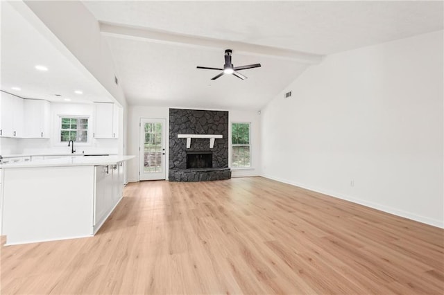 unfurnished living room with a ceiling fan, a fireplace, lofted ceiling with beams, light wood-style flooring, and a wealth of natural light