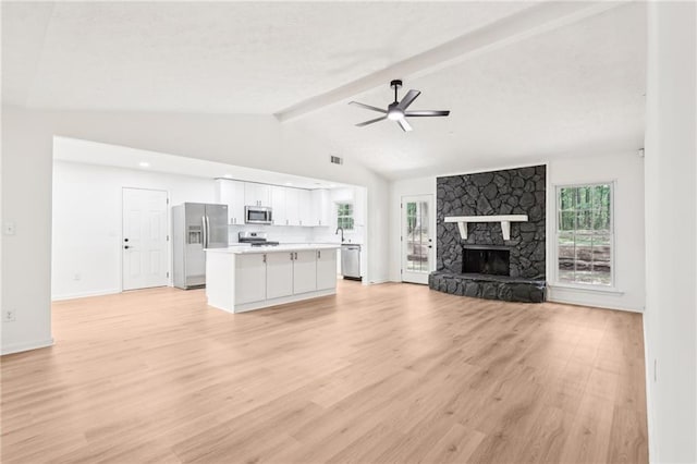 unfurnished living room featuring ceiling fan, a stone fireplace, light wood-type flooring, a sink, and lofted ceiling with beams