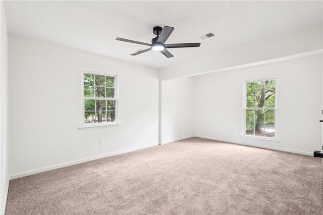 carpeted spare room featuring visible vents, a ceiling fan, baseboards, and a wealth of natural light