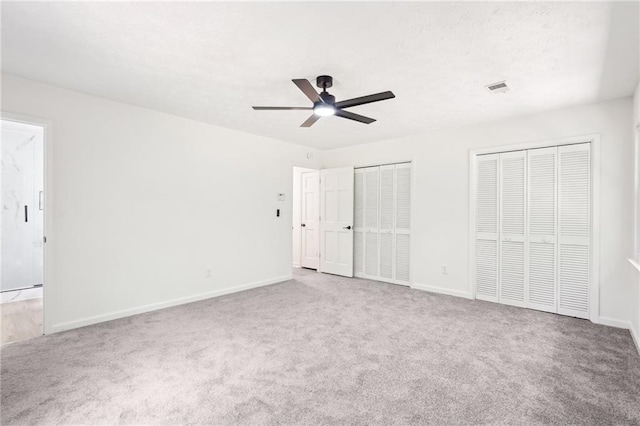 unfurnished bedroom with visible vents, carpet flooring, baseboards, and two closets