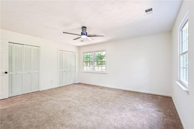 unfurnished bedroom featuring carpet floors, multiple closets, multiple windows, and visible vents