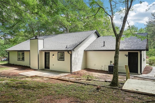 back of house featuring a shingled roof, a patio area, a chimney, and central AC unit