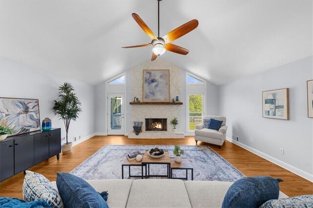 living room with a ceiling fan, a stone fireplace, lofted ceiling, and wood finished floors