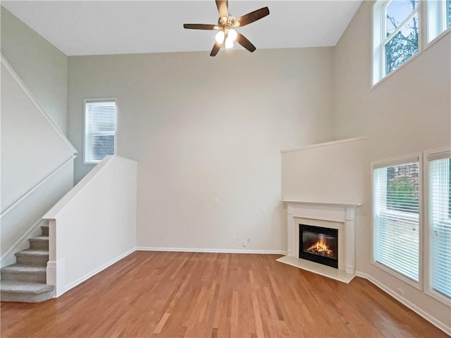 unfurnished living room featuring a towering ceiling, ceiling fan, and light hardwood / wood-style floors