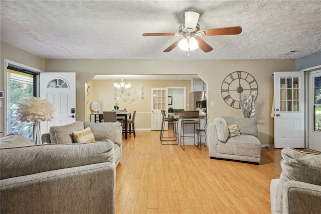 living room featuring ceiling fan with notable chandelier, a textured ceiling, and light wood-type flooring