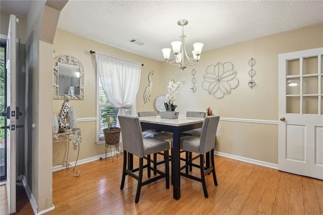 dining room featuring a textured ceiling, light hardwood / wood-style floors, and an inviting chandelier