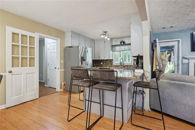 kitchen with tasteful backsplash, stainless steel fridge with ice dispenser, kitchen peninsula, a textured ceiling, and light wood-type flooring