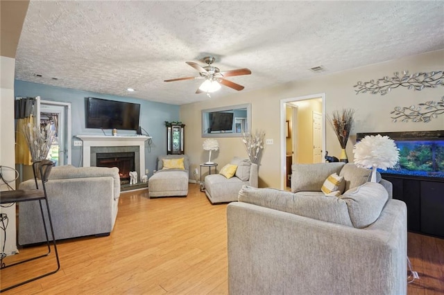 living room featuring ceiling fan, light hardwood / wood-style floors, a textured ceiling, and a tile fireplace