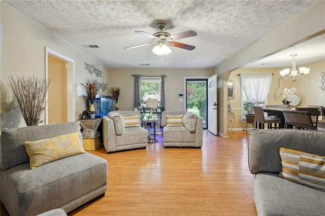 living room featuring light hardwood / wood-style flooring, ceiling fan with notable chandelier, and a textured ceiling