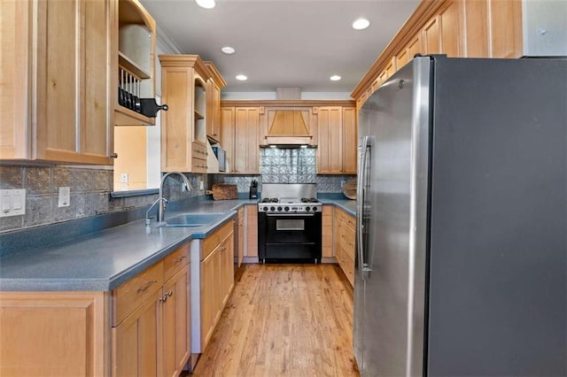 kitchen featuring custom exhaust hood, gas range, sink, light hardwood / wood-style flooring, and stainless steel refrigerator