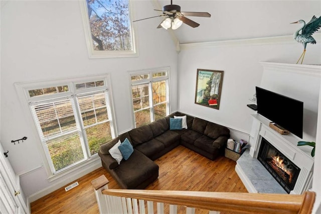 living room featuring ceiling fan, a high ceiling, crown molding, wood-type flooring, and a fireplace