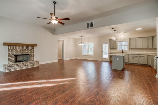 unfurnished living room with ceiling fan with notable chandelier, a fireplace, a sink, visible vents, and dark wood finished floors