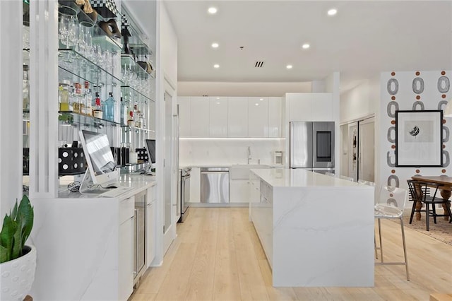 kitchen featuring white cabinetry, a center island, a breakfast bar, appliances with stainless steel finishes, and light wood-type flooring