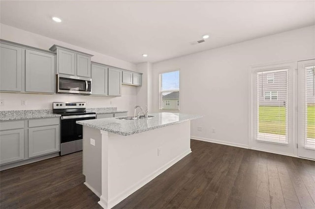kitchen featuring gray cabinetry, a center island with sink, a sink, dark wood finished floors, and stainless steel appliances
