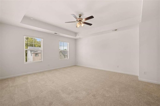 spare room featuring a tray ceiling, light colored carpet, baseboards, and ceiling fan