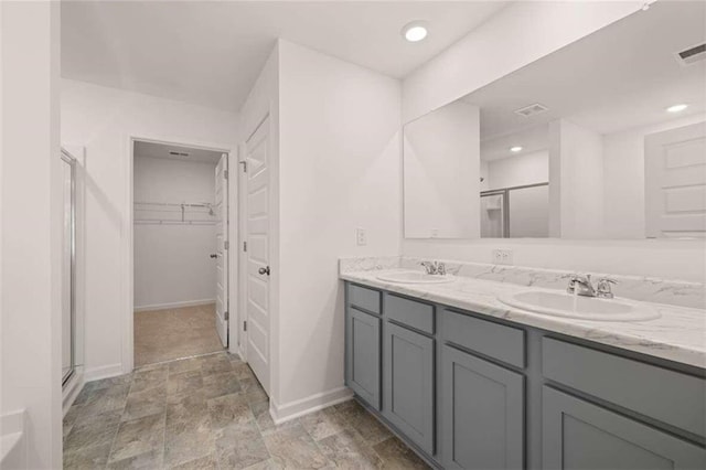 bathroom with double vanity, a stall shower, a walk in closet, and a sink