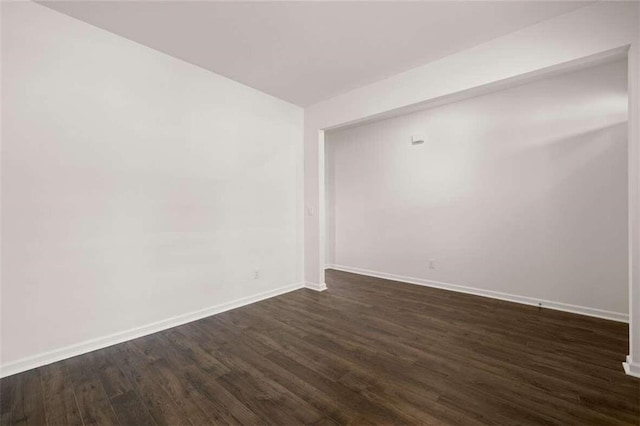 spare room featuring baseboards and dark wood-style flooring