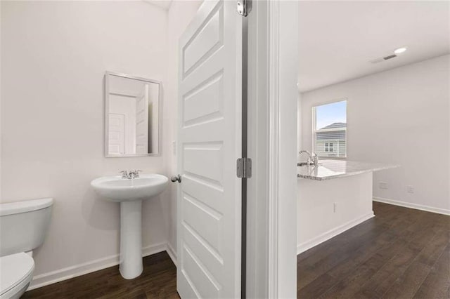 half bath with visible vents, toilet, baseboards, and wood finished floors