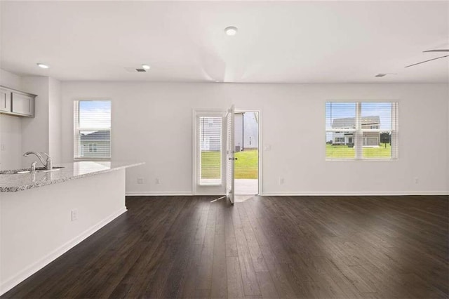 unfurnished living room with dark wood-style flooring, baseboards, and a sink